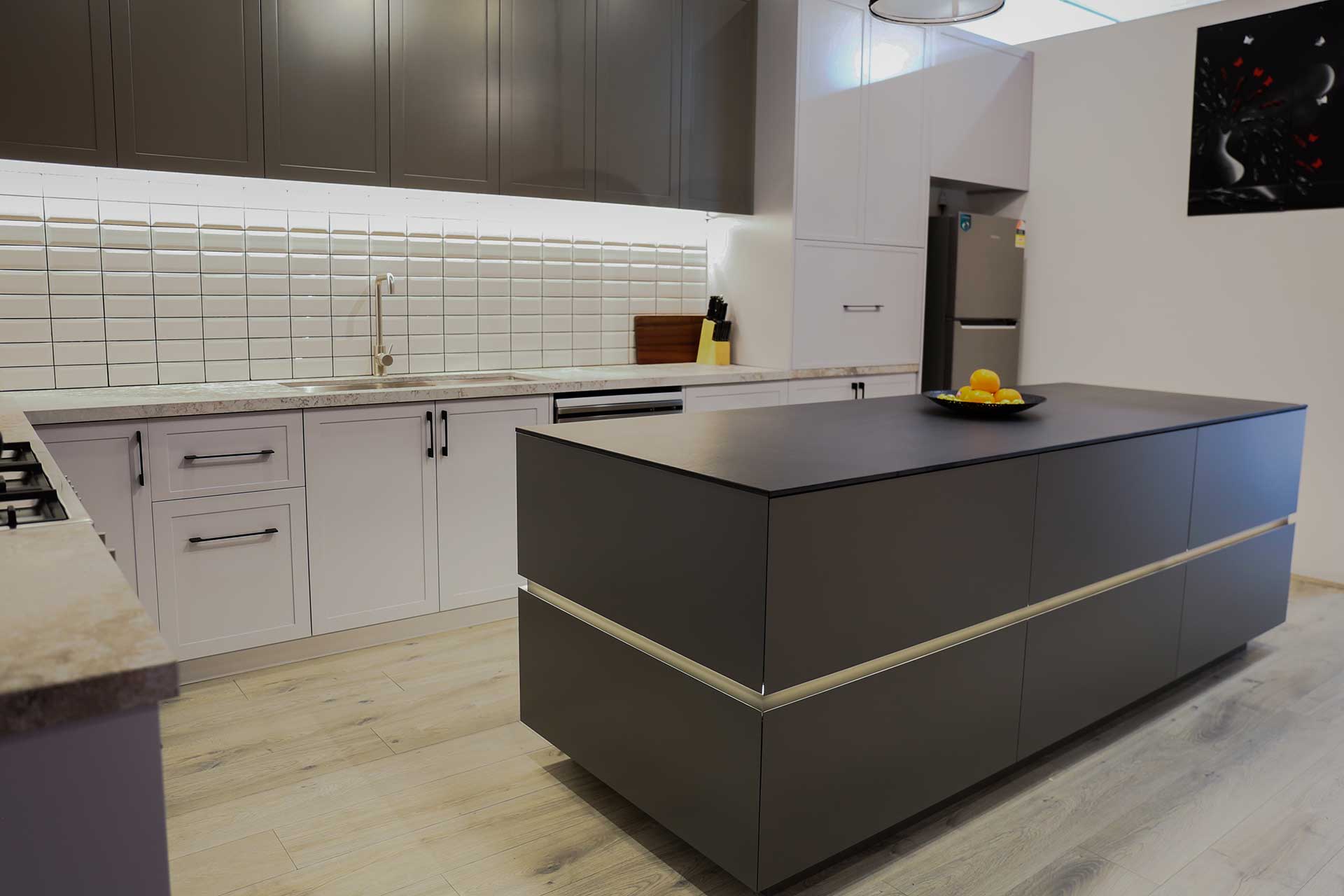 Modern kitchen with a large black island, white cabinets, stainless steel appliances, and a fruit bowl on the counter.