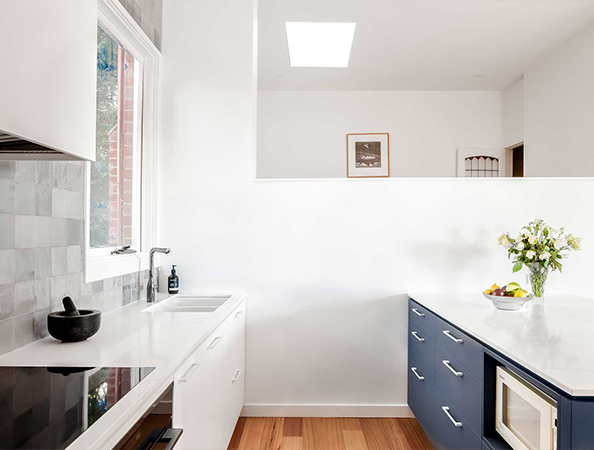 Minimalist kitchen with white and blue cabinets, wooden floor, and a vase with flowers on the counter.