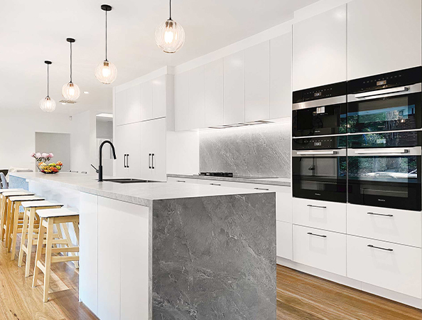 Modern kitchen with white cabinets, marble island, and pendant lights. Wooden stools line the bar area. Modern kitchen with white cabinets, marble island, and pendant lights. Wooden stools line the bar area.