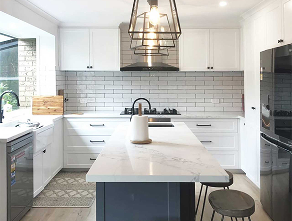 Modern kitchen with white cabinets, marble island, black fixtures, and pendant lighting over the island.