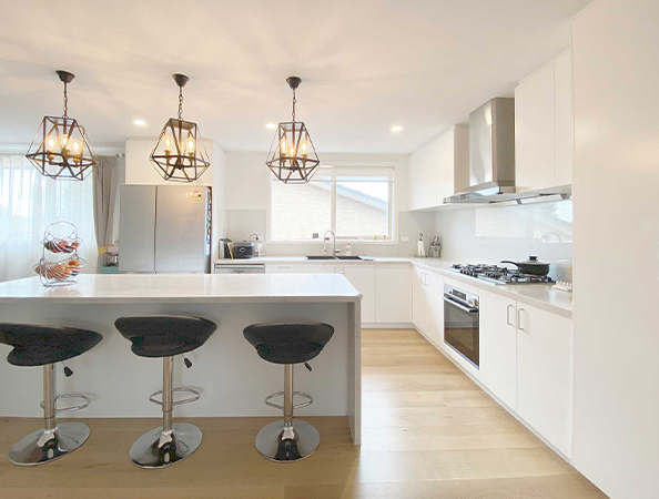 Modern kitchen with white cabinets, island, and three stools. Pendant lights hang above the island.