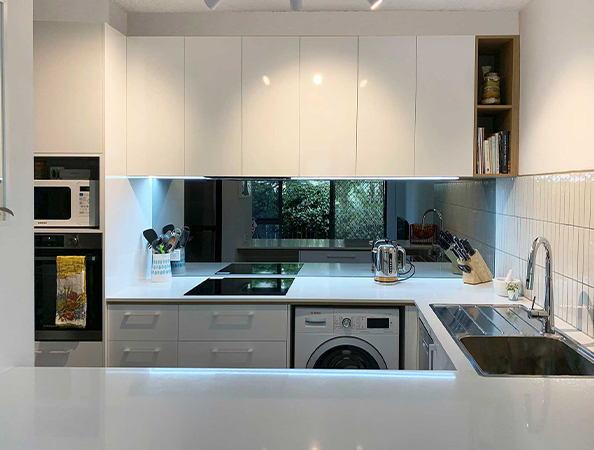 Modern kitchen with white cabinets, built-in oven, induction cooktop, washing machine, and stainless steel sink.