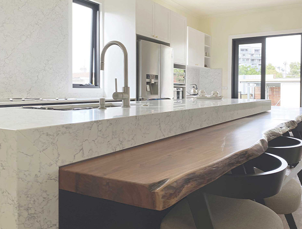 Modern kitchen with marble countertops, large wooden island, stainless steel appliances, and bright windows.