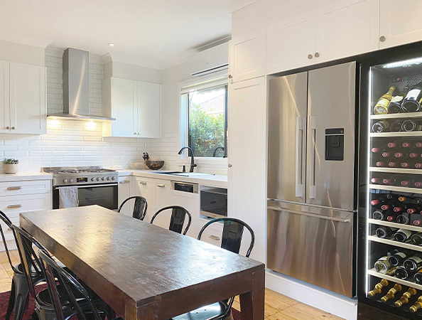 Modern kitchen with a wooden dining table, black chairs, stainless steel appliances, and a wine cooler.