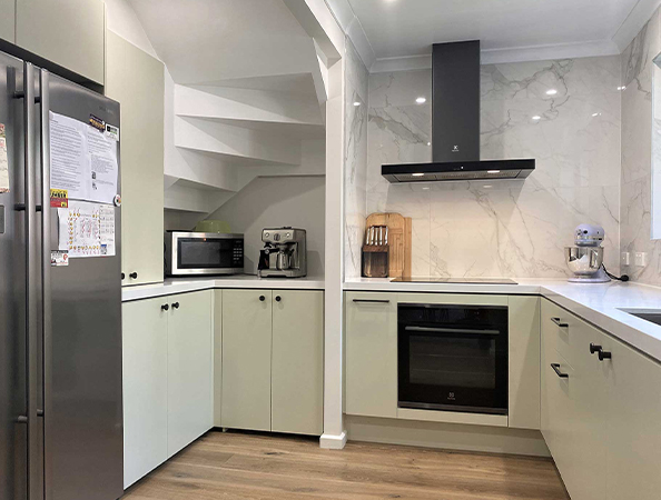 Modern kitchen with light cabinets, oven, microwave, and refrigerator. Marble backsplash and hardwood floor.