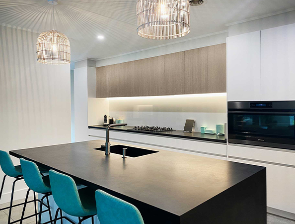 Modern kitchen with island, sleek black countertop, teal barstools, pendant lights, and built-in oven. Modern kitchen with island, sleek black countertop, teal barstools, pendant lights, and built-in oven.