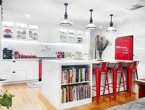 Modern kitchen with a red refrigerator, white cabinets, an island with bookshelves, and red bar stools. Modern kitchen with a red refrigerator, white cabinets, an island with bookshelves, and red bar stools.