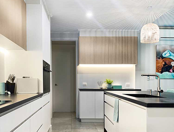 Modern kitchen with light wood cabinets, black countertops, and a hanging light fixture above an island.