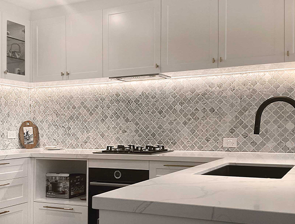 Modern kitchen with white cabinets, patterned backsplash, black faucet, and under-cabinet lighting. Modern kitchen with white cabinets, patterned backsplash, black faucet, and under-cabinet lighting.
