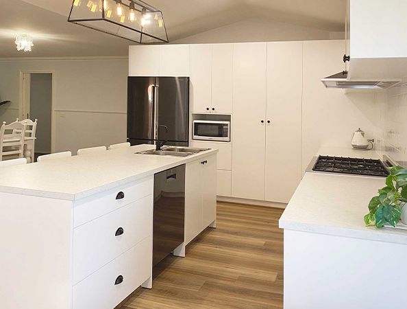 Modern kitchen with white cabinets, island counter, stainless steel fridge, microwave, and hardwood floor.