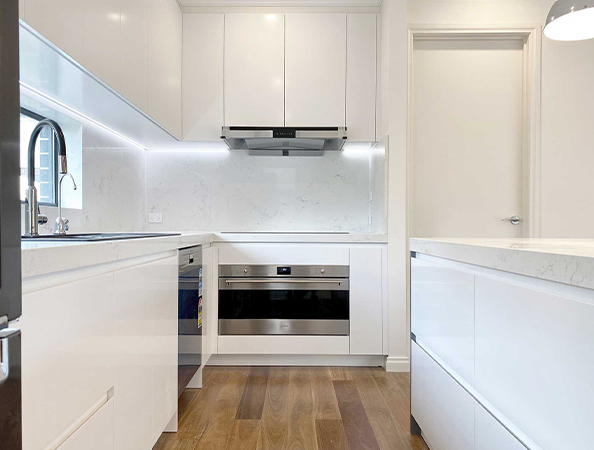 Modern kitchen with white cabinets, stainless steel appliances, marble countertops, and wooden floor. Modern kitchen with white cabinets, stainless steel appliances, marble countertops, and wooden floor.