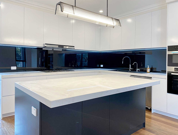 Modern kitchen with white cabinets, black backsplash, and a large island with white countertop under a sleek light fixture.