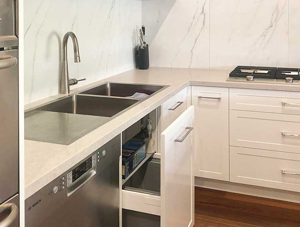 Modern kitchen with stainless steel sink, dishwasher, white cabinets, and a gas stove on light countertops. Modern kitchen with stainless steel sink, dishwasher, white cabinets, and a gas stove on light countertops.