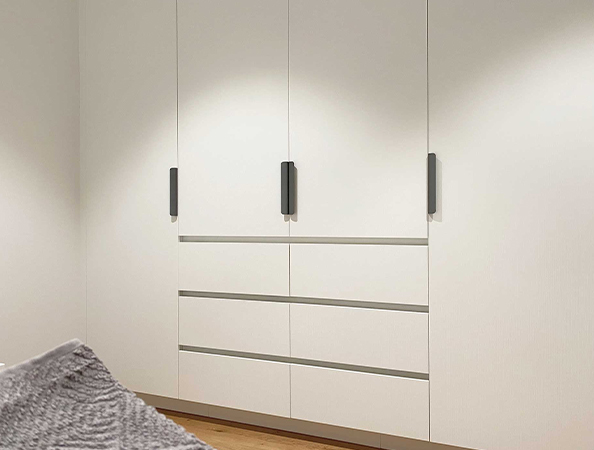 White built-in wardrobe with black handles, featuring three tall doors and four horizontal drawers.