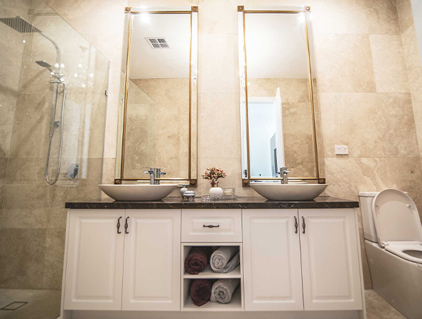 Bathroom with twin sinks, large mirrors, and white cabinetry. Includes a shower, towels, and a toilet on the right.