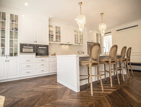 Spacious kitchen with wood flooring, white cabinets, island with stools, and two ornate chandeliers.