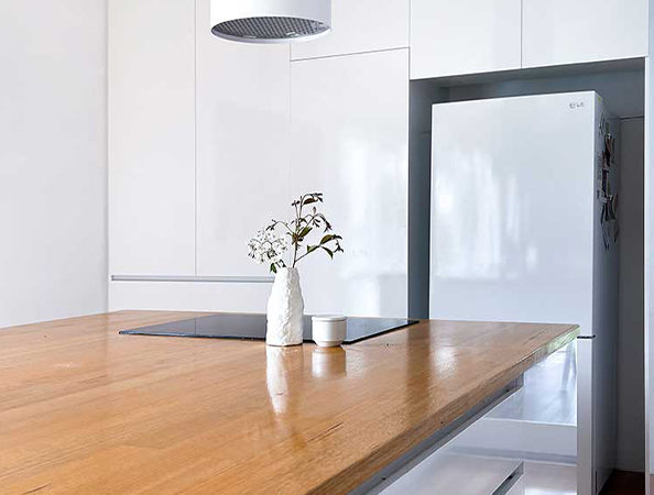 Minimalist kitchen with wooden countertop, white cabinets, white fridge, and small vase with flowers.