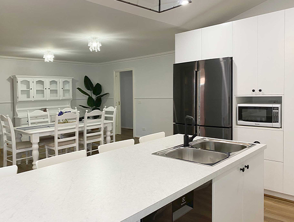Modern kitchen with a white island, stainless steel appliances, and a dining table in the background.