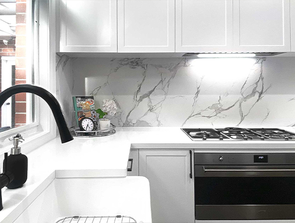 Modern kitchen with marble backsplash, sleek white cabinets, black faucet, and a stainless steel gas stove.