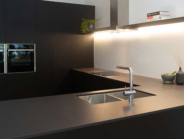 Modern kitchen with sleek black cabinets, under-cabinet lighting, and a steel sink with a chrome faucet.