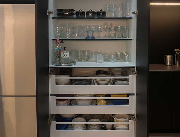A kitchen cabinet open to show neatly arranged glassware and dishware on shelves and drawers.