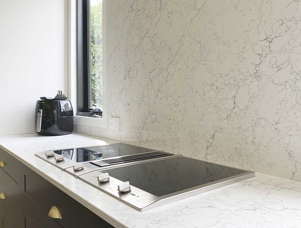 Modern kitchen with white marble countertop, electric stovetop, black air fryer, and large window.