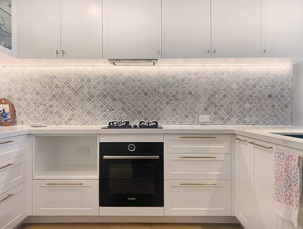 Modern kitchen with white cabinets, patterned backsplash, black oven, and gas stove. Tea towel on dishwasher handle.