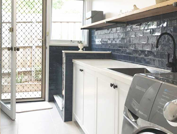 Laundry room with a washing machine, white cabinetry, dark blue brick backsplash, and a screen door. Laundry room with a washing machine, white cabinetry, dark blue brick backsplash, and a screen door.