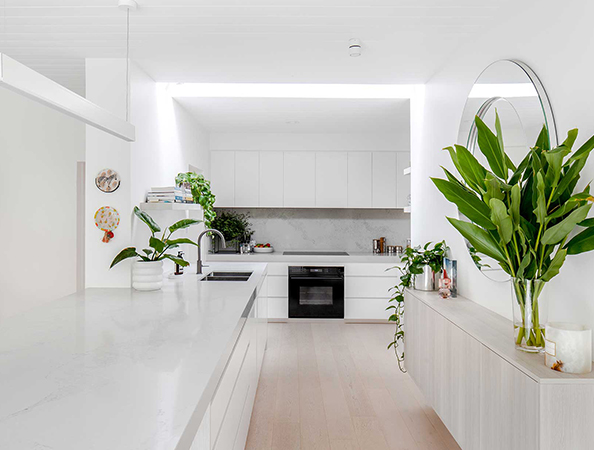 Bright, modern kitchen with white cabinetry, large plants, round mirror, and sleek countertops. Bright, modern kitchen with white cabinetry, large plants, round mirror, and sleek countertops.