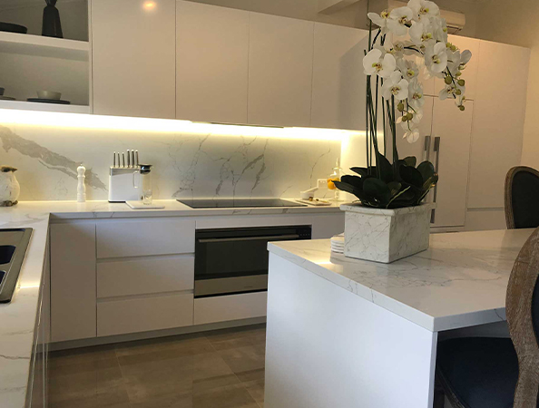 Modern kitchen with white cabinets, marble countertops, and a potted orchid on the island. Bright under-cabinet lighting. Modern kitchen with white cabinets, marble countertops, and a potted orchid on the island. Bright under-cabinet lighting.