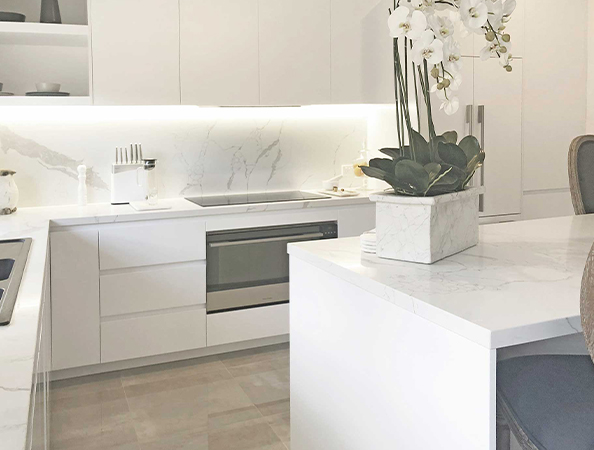 Modern white kitchen with marble countertops, an induction cooktop, and a potted orchid on the island. Modern white kitchen with marble countertops, an induction cooktop, and a potted orchid on the island.