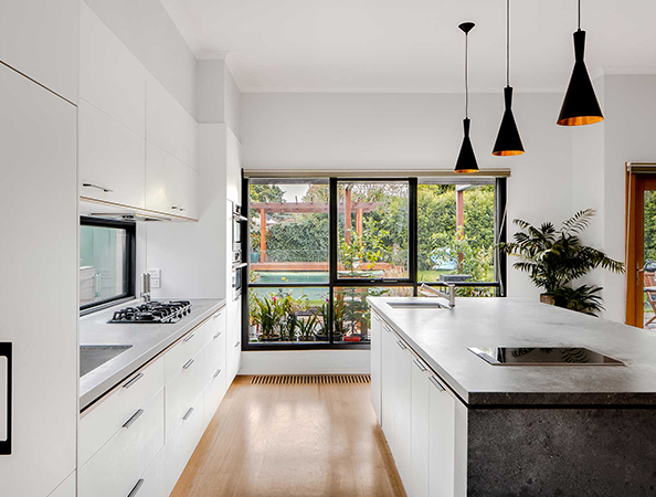 Modern kitchen with white cabinets, large windows, an island, and hanging black pendant lights.