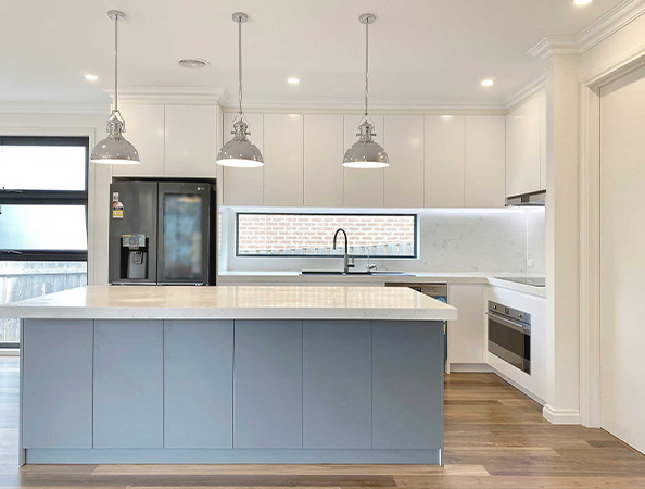 Modern kitchen with a large island, pendant lights, white cabinets, and a stainless steel refrigerator.
