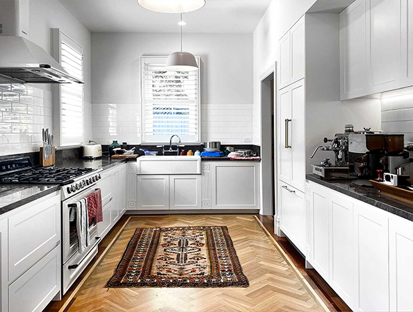 Modern kitchen with white cabinets, a farmhouse sink, stainless steel appliances, and a patterned rug on wooden floor.
