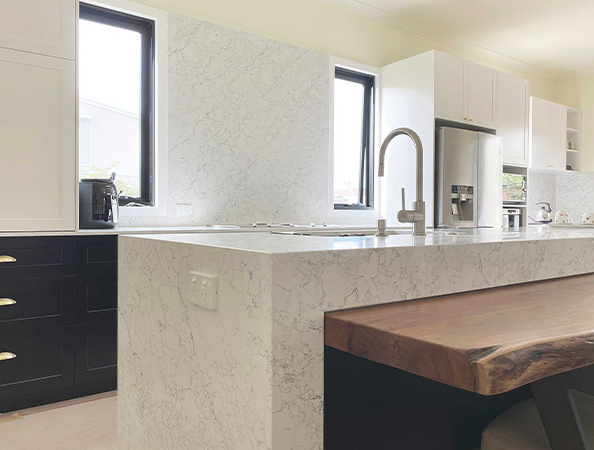 Modern kitchen with a marble island countertop, wooden bench, black lower cabinets, and stainless steel appliances.