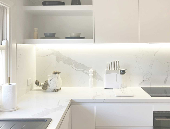 Bright white kitchen with marble counters, black stove, knife set, and decorative bird on counter near window.