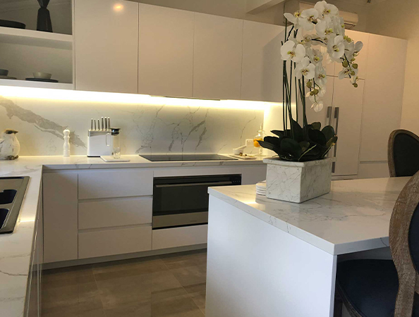 Modern kitchen with white cabinets, marble countertops, and a potted orchid on the island.