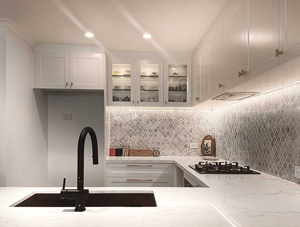 Modern kitchen with white cabinets, marble countertops, black faucet, and patterned backsplash.