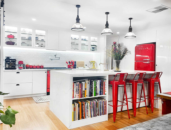 Modern kitchen with white cabinets, red fridge, red bar stools, and a white island with books and flowers. Modern kitchen with white cabinets, red fridge, red bar stools, and a white island with books and flowers.