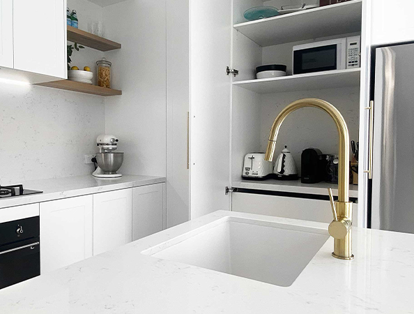 Modern kitchen with a white countertop, gold faucet, and open shelving with appliances like a mixer and toaster.