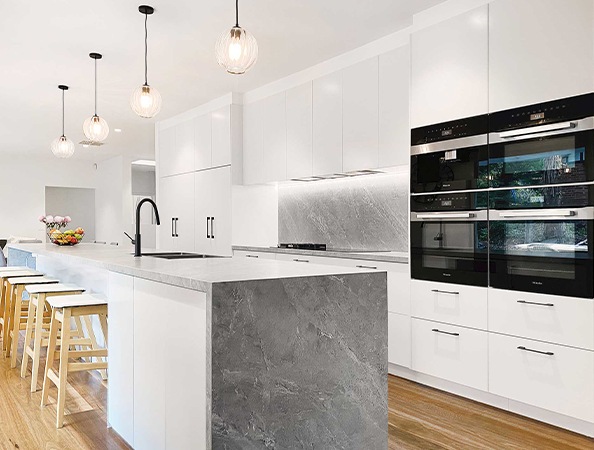 Modern kitchen with white cabinets, gray countertops, an island with stools, and hanging pendant lights.