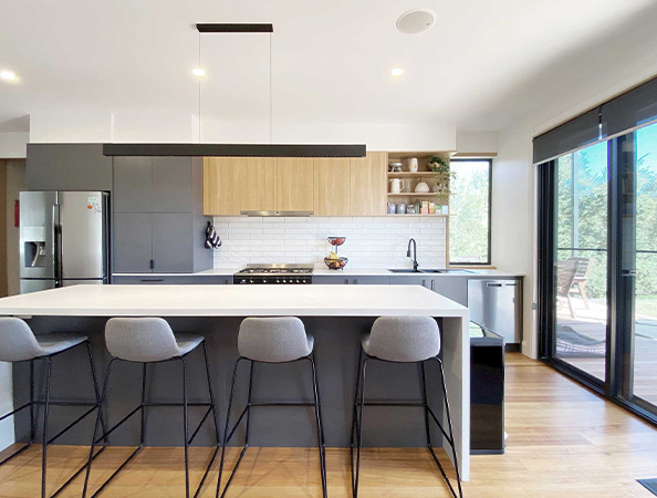 Modern kitchen with a large island, gray stools, open shelving, and large windows with a view outside.