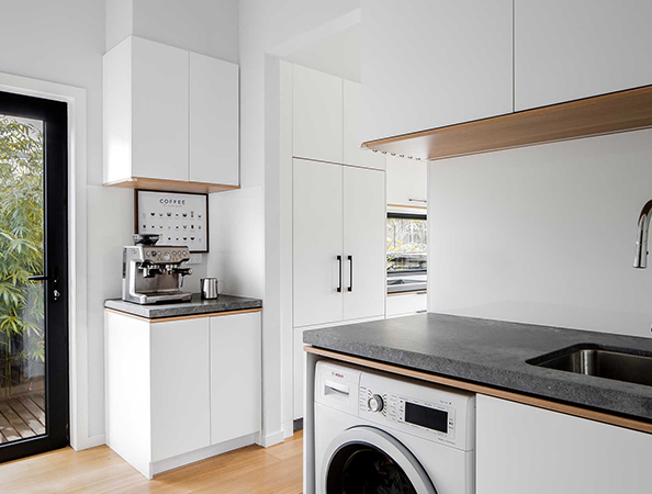 Minimalist kitchen with a washing machine, sink, and coffee machine on a black countertop.