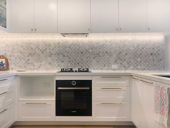 Modern white kitchen with marble backsplash, gas stove, oven, and under-cabinet lighting. Towel on the right. Modern white kitchen with marble backsplash, gas stove, oven, and under-cabinet lighting. Towel on the right.