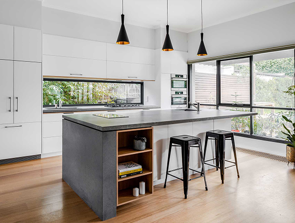 Modern kitchen with a large island, bar stools, pendant lights, white cabinets, and a large window with garden view.