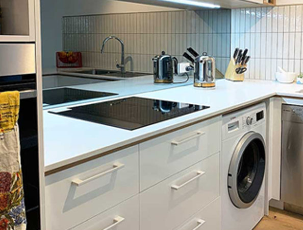 Modern kitchen corner with white cabinets, stovetop, oven, washing machine, knives, and toaster on counter.
