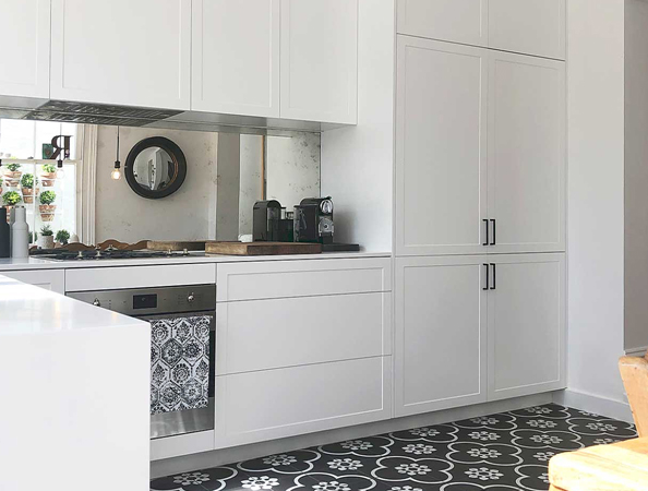 Modern kitchen with white cabinets, patterned tile floor, a round mirror, and small plants on the counter.