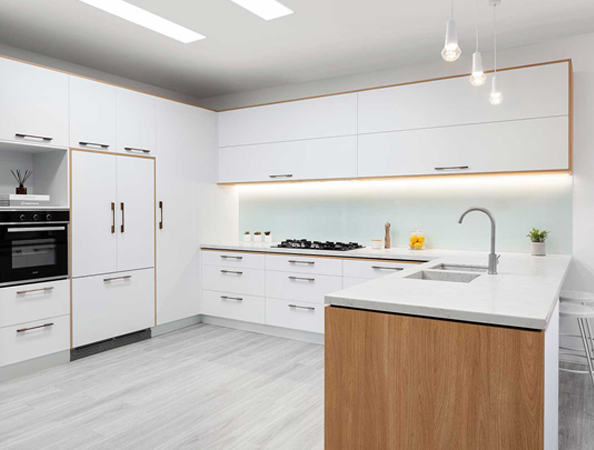 Modern kitchen with white cabinets, built-in oven, cooktop, and wooden island with a sink under hanging lights.