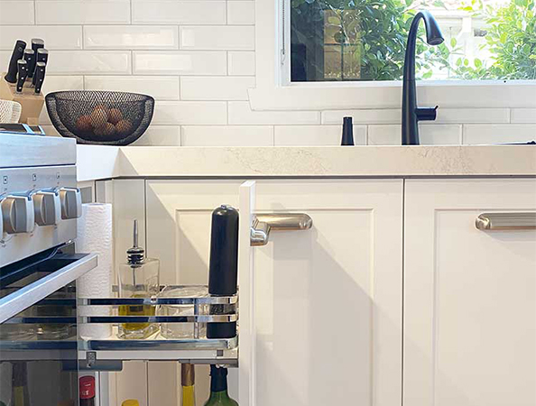 Kitchen with open cabinet displaying spices, utensils, and a wine bottle. Black faucet and knife set visible on counter. Kitchen with open cabinet displaying spices, utensils, and a wine bottle. Black faucet and knife set visible on counter.