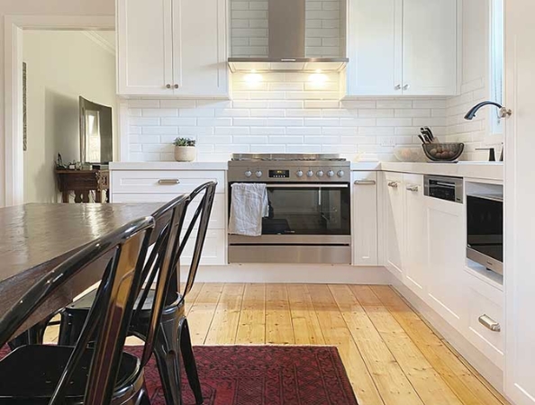 Modern kitchen with white cabinets, stainless steel appliances, and a wooden floor. Red rug and black chairs by the table. Modern kitchen with white cabinets, stainless steel appliances, and a wooden floor. Red rug and black chairs by the table.